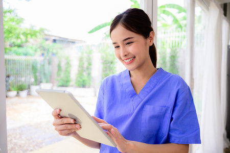 Portrait of happy doctor or nurse caregiver holding tablet visiting patient in hospital or nursing home, Female doctor caregiver wearing uniform checking and working with medical treatmentの写真素材