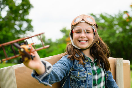 Happy girl playing with cardboard toy airplane handicraft in garden