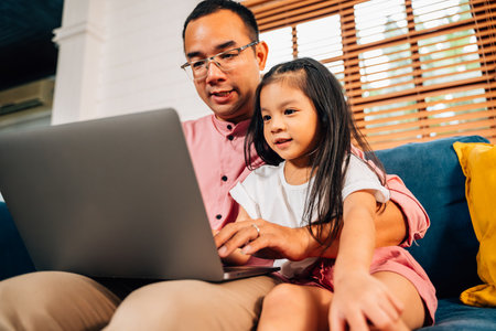 Father using laptop playing with daughter in living roomの写真素材