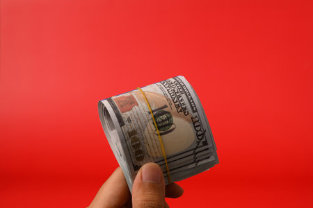 Hand holding hundred dollar bills on red background, Banknotes for money saving, Cash money dollars,...