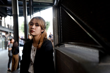 Blond hair woman in half-tied hairstyle standing next to the structure of shopping mall lots of people in daytime of weekend.の写真素材