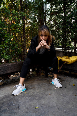 Blond hair woman in black suit sitting with wide legs on the wooden log prop her elbows on the knees...
