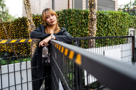 Blond hair woman prop her arms on the black fence in front of the garden with decorated light.の写真素材
