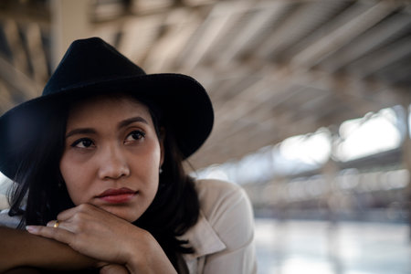 Wavy hair woman with black hat rest her hands on the bench's backrest and prop her head on hands...