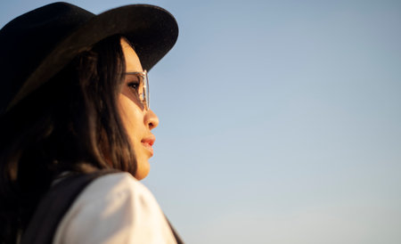 Wavy hair woman with black hat and sunglasses look at the sunlight in the evening with the sky as a background.の写真素材