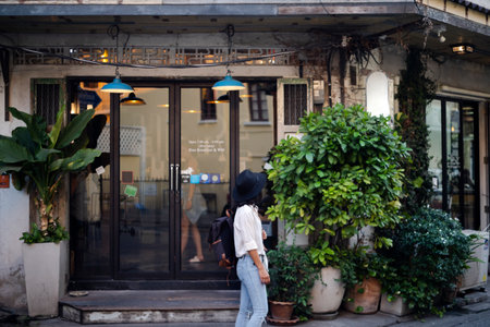 White shirt woman wearing black hair stop walking in front of the minimal hostel with lots of tree at front, she's very interested in this hostel.の写真素材