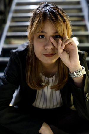 Blond hair woman in black and white clothes sitting on the stair and making V sing then smile.の写真素材