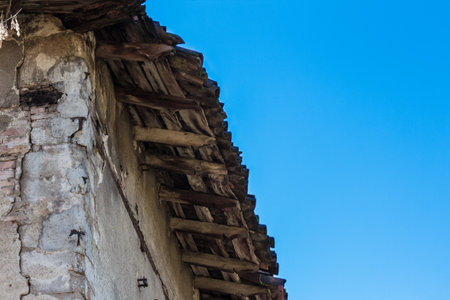 damaged roof of an old house, seen from below with blue sky in the backgroundの写真素材