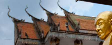 Golden Buddha with beautiful ancient temple in Laos under a cloudy but blue skyの写真素材