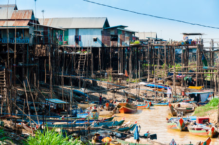 House on stilts and wooden boats at muddy river in Cambodiaの写真素材