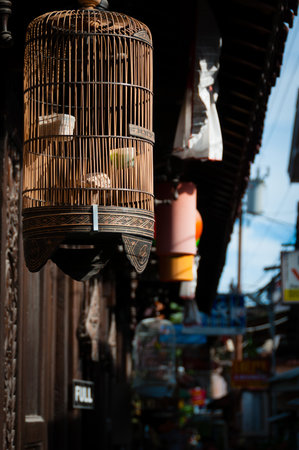A bird cage hanging off a roof on a small street in Indonesiaの写真素材