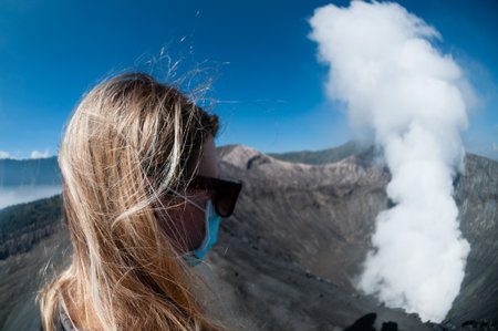 Blond haired Woman watching volcano Bromo smoking under blue sky in Indonesiaの写真素材