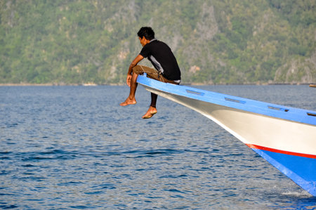 Man Sitting in the front of a wooden boat near Coron, Palawan, Philippinesの写真素材