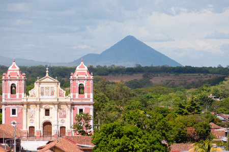 Big Pink Church Standing in front of a Mountain volcano and trees in Leon in Nicaraguaの写真素材