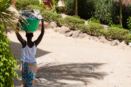 African woman carrying bucket on her head in dust street of Dakar, Senegalの写真素材