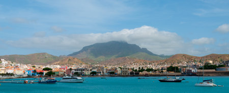 Boats in front of small town at the blue ocean coast with cloudy mountain background, Cape Verde...