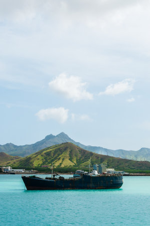 Old rusty Ship in the blue ocean at coast with cloud and green mountain background, Cape Verde...