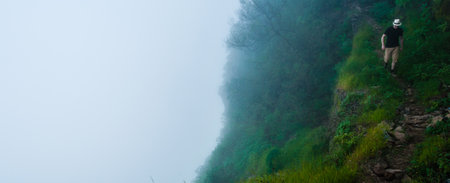 White man with black shirt and hat walking along a deep foggy misty cliff above the clouds on...