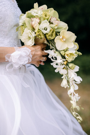 Bride holding the wedding bouquet with white flowers on white wedding dressの写真素材