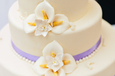 Marzipan flowers and purple ribbon on wedding cake with white flower decorationの写真素材