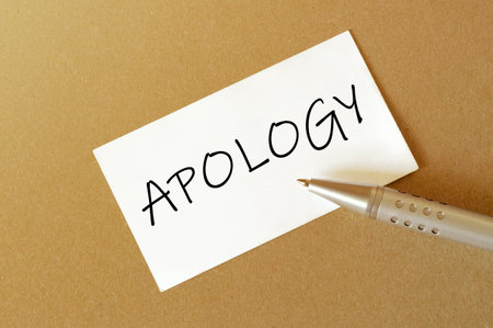 pen, white paper with text APOLOGY on the brown backgroundの写真素材