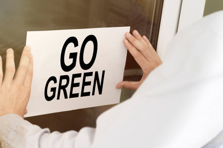 a man hangs a notice on a glass door with the text Go Greenの写真素材