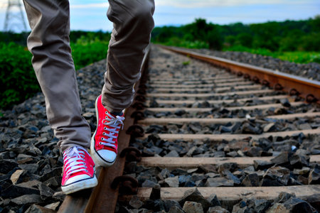 A man wearing red shoes and walking on the railway trackの写真素材