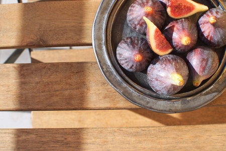 Fresh figs on ceramic black plate Wooden table Sunligh Copy space Autumn harvesting Fall Top view