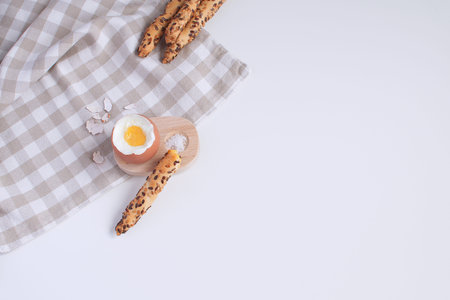 Served breakfast boiled egg in wooden egg cup with breadsticks salt spoon and checkered napkin White...