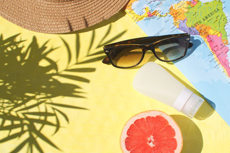 Travel concept Summer season Adventure Female accessories Flat lay Sunglasses Sunscreen Half ripe grapefruit Straw hat World map yellow background Top view Copy space Tropical leaf shadowの写真素材