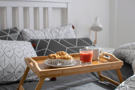 Christmas morning, Valentines day, cozy morning, horel room - breakfast in bed, wooden tray with coffee, muffins, orange juice on the bed. Modern minimal scandinavian bedroom interior. Copy space.の写真素材