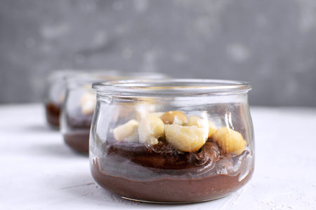Healthy eating - vegan chocolate pudding made from avocado in glass jar with macadamia nuts on top, close-up, white background, copy space. Menu designの写真素材