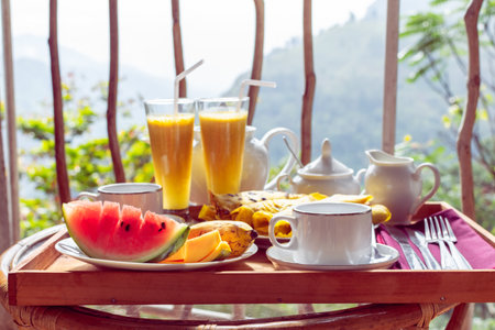 Beautifully served breakfast on terrace or balcony, hotel room, resort - fresh watermelon, mango, banana, smoothie, pancakes, teapot, cups, rattan chairの写真素材
