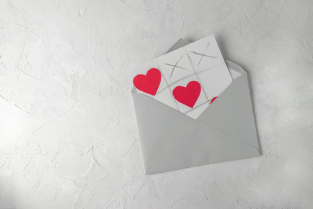 Valentine day handmade greetings card - tic tac toe game with hearts, grey envelope, white concrete backgroundの写真素材