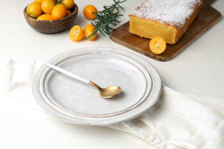 Served plate, spoon with orange cake on wooden cutting board, fresh kumquats - homemade bakeryの写真素材