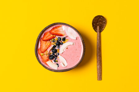 Spring diet, body detox, healthy breakfast concept, lifestyle blog - coconut bowl with fruit smoothie, fresh strawberries, blueberries, coconut chips, top view, yellow backgroundの写真素材