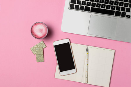 Workspace of freelancer, blogger, journalist - laptop, notepad, pen, cup of trendy superfood pink beetroot latte, chocolate, smartphone on pastel pink background, flat lay, copy spaceの写真素材