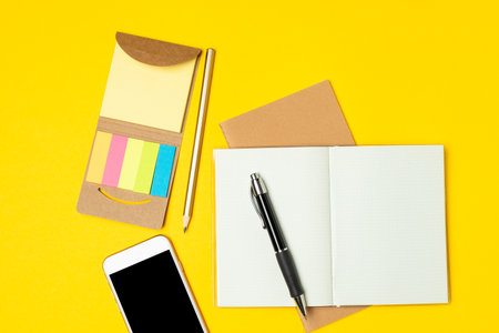 Business, planning concept - Work place, notepad, sticky notes, smartphone and pen on bright yellow background, flat layの写真素材