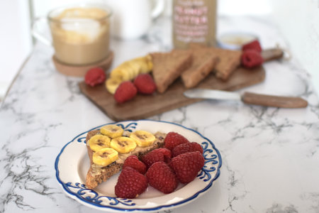 Healthy breakfast - peanut butter sandwich, banana, raspberry, cappuccino coffee, marble table backgroundの写真素材
