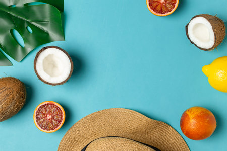 Bright blue summer background flat lay, copy space - tropical fruits, blood oranges, coconut, straw hat, monstera leafの写真素材