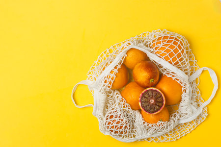 Organic bloody oranges in cotton mesh reusable shopping bag, yellow background, top view - recycling, sustainable lifestyle, zero waste, no plasticの写真素材