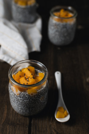 Chia pudding in glass jar with almond milk and mango on rustic wooden table - healthy superfood vegan breakfastの写真素材