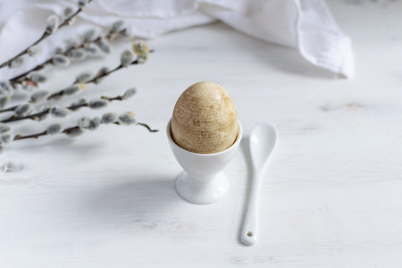 Naturally dyed easter egg for breakfast, white egg cup, draped napkin, white wooden table, willow banch - minimal easter concept, copy spaceの写真素材