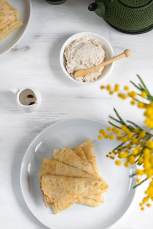 Morning, breakfast - traditional russian blini pancakes, french crepes whipped cream, cast iron green teapot, mimosa flower, white wooden table, top viewの写真素材