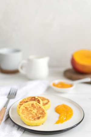 Traditional russian syrniki or cottage cheese pancakes served with mango, coffee, milk pitcher, healthy protein breakfast, copy spaceの写真素材