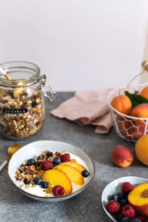 Granola with greek yogurt fresh peach, blueberry, raspberry on the table - healthy breakfast conceptの写真素材