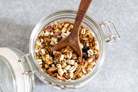 Granola with pecan nuts in glass jar on gray table, selective focus, top view, copy space - healthy diet breakfastの写真素材