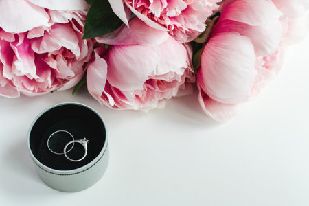 Wedding invitation concept - rings, envelope, pink peonies flowers on white background, copy spaceの写真素材