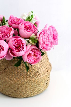 Bouquet of beautiful pink peonies in straw basket, white background, copy space, wedding flowersの写真素材