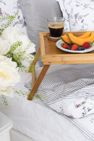 Romantic breakfast in bed - wooden tray with fresh fruits and espresso coffee, peony flowers